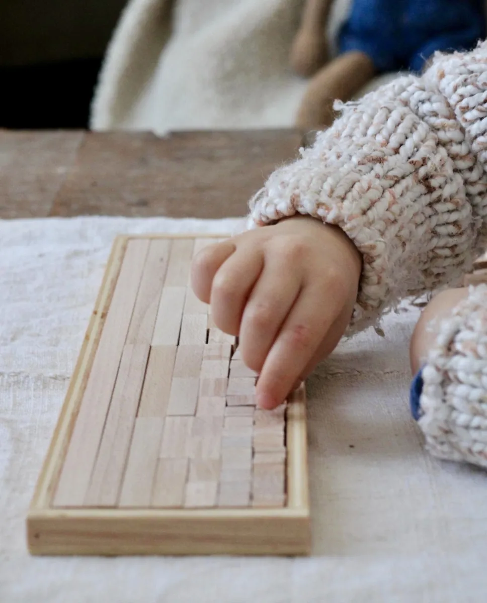 Main d'enfant manipulant un plateau pédagogique en bois Serclet